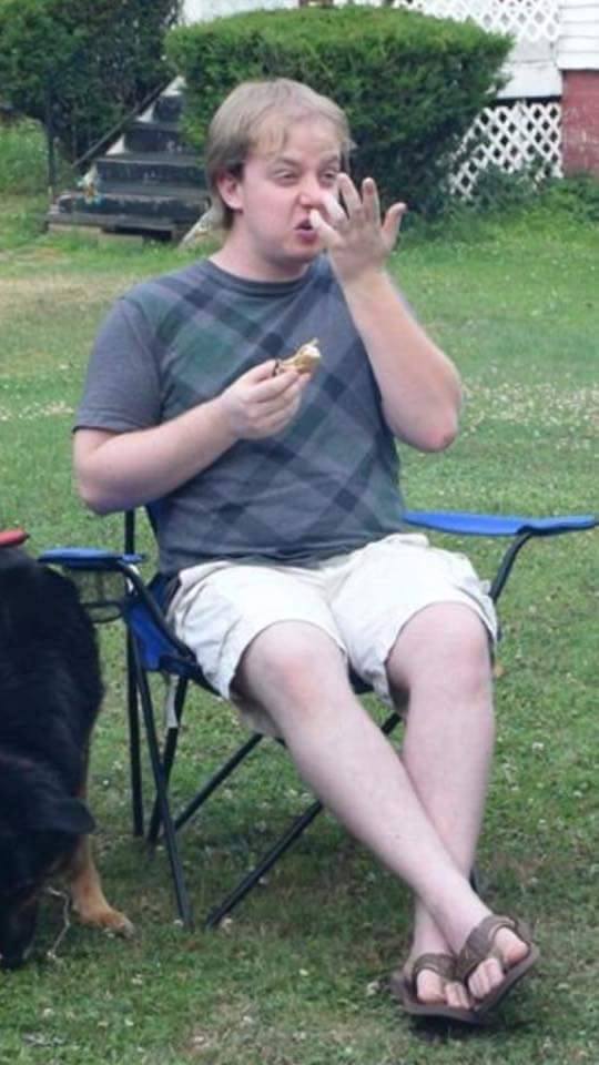 a photograph of luke wenke sitting outdoors and sniffing his fingers.